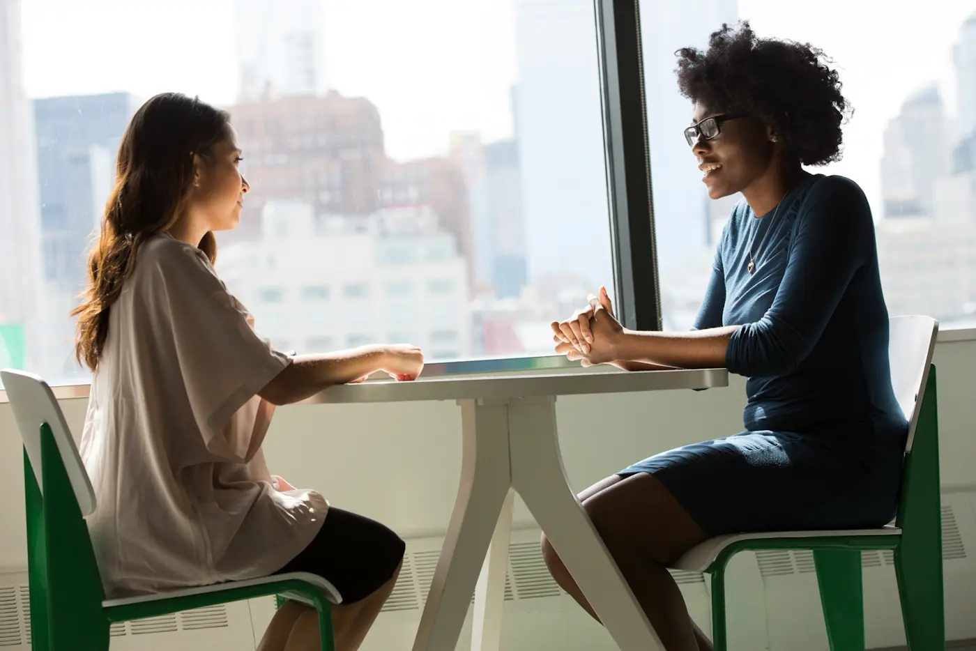Two women talking at a table by a window